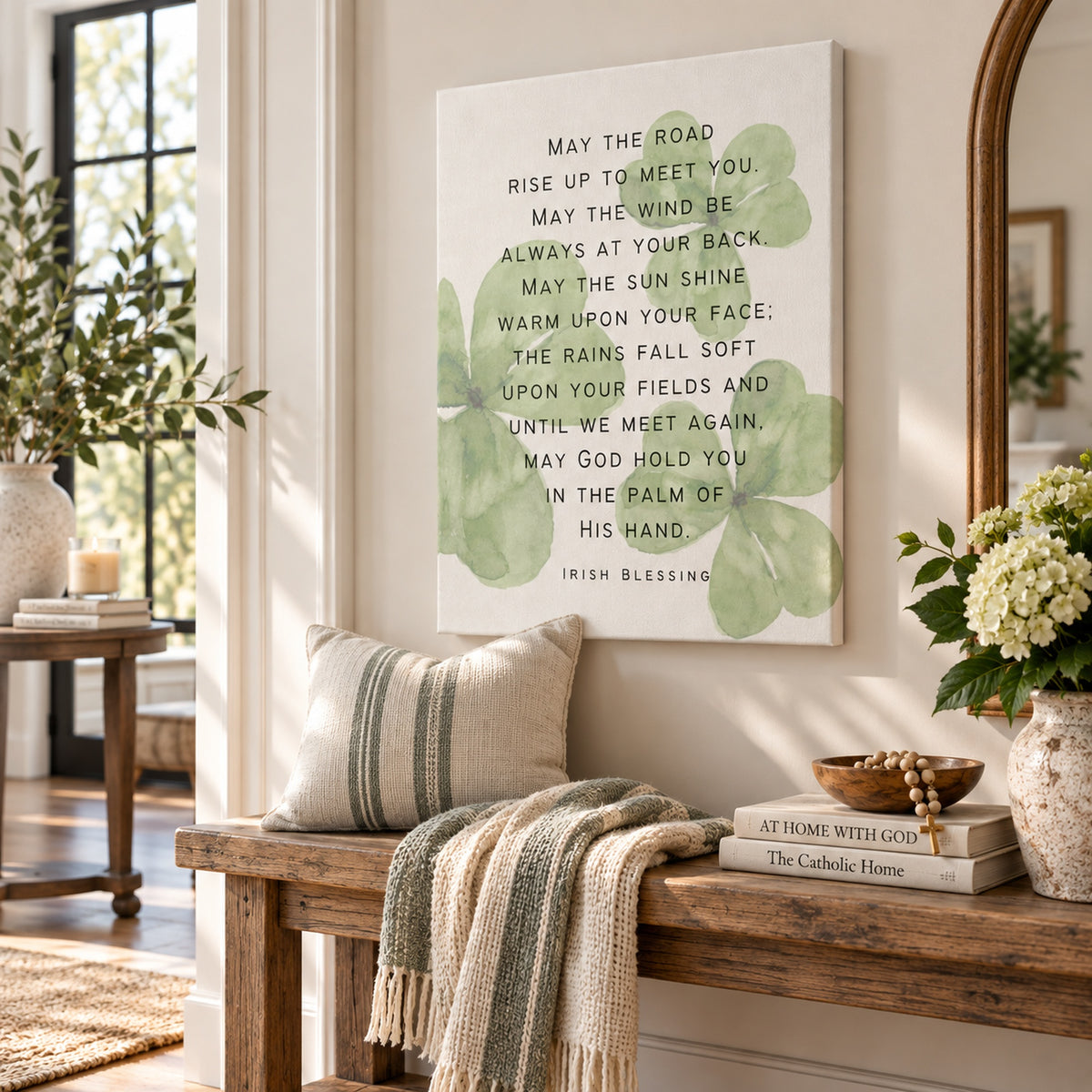 A square canvas wall art print featuring the Irish Blessing poem in black text over a white background with soft green leaf motifs, displayed in a bright, modern entryway above a wooden bench with a striped pillow and throw blanket.